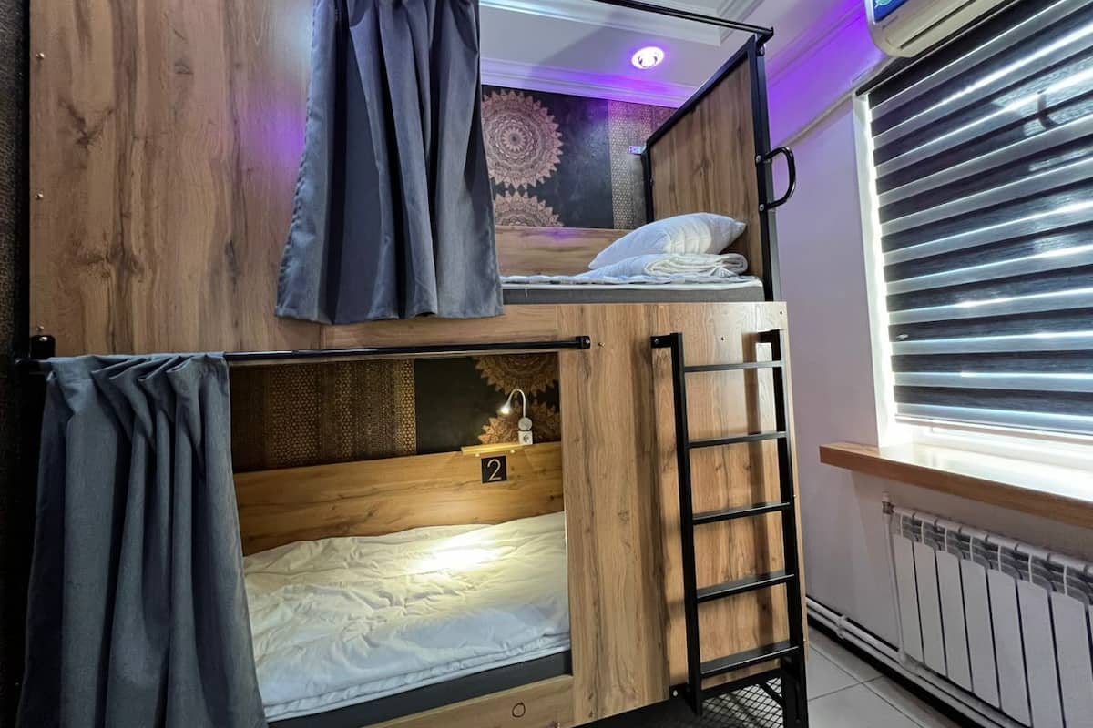 Ein Schlafraum mit Etagenbett, einer Leiter, einem Fenster mit Jalousien und einer Deckenleuchte.