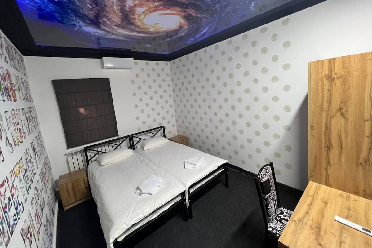 Ein Schlafzimmer mit Bett, Schreibtisch, Stuhl, einer Wand-Klimaanlage und einer Decke mit einem Galaxienbild.