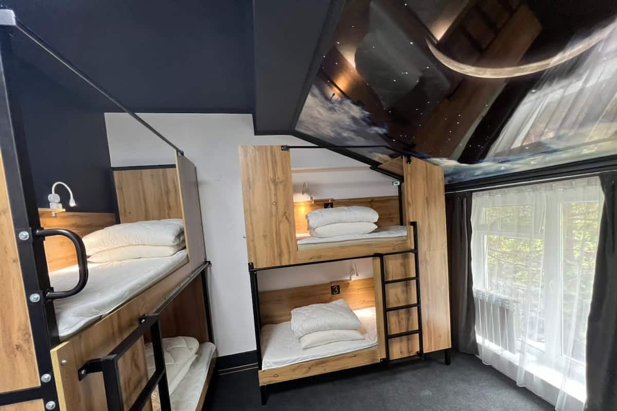 Ein Schlafraum mit Etagenbetten, einem Sternenhimmel-Design, einem Fenster mit Vorhängen und einer Holzleiter.