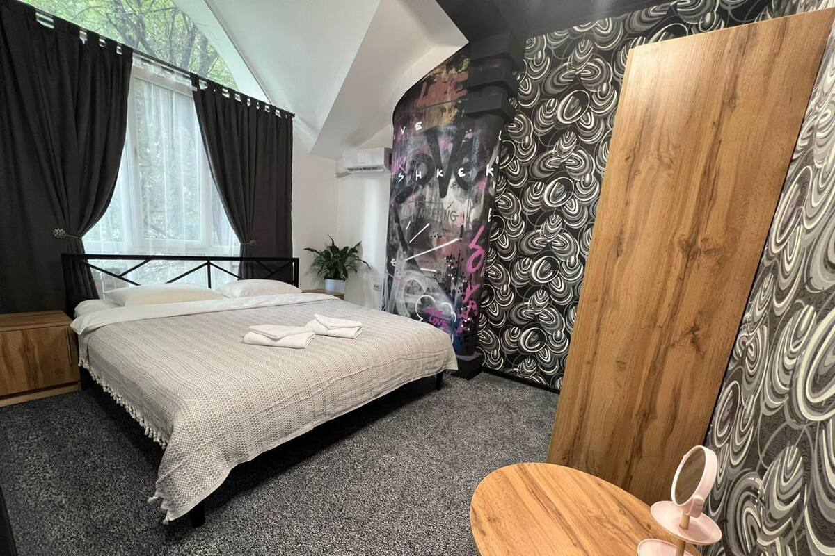 Ein Schlafzimmer mit einem Bett, einem Holzstuhl, einem Spiegel und einem Fenster mit Vorhängen.