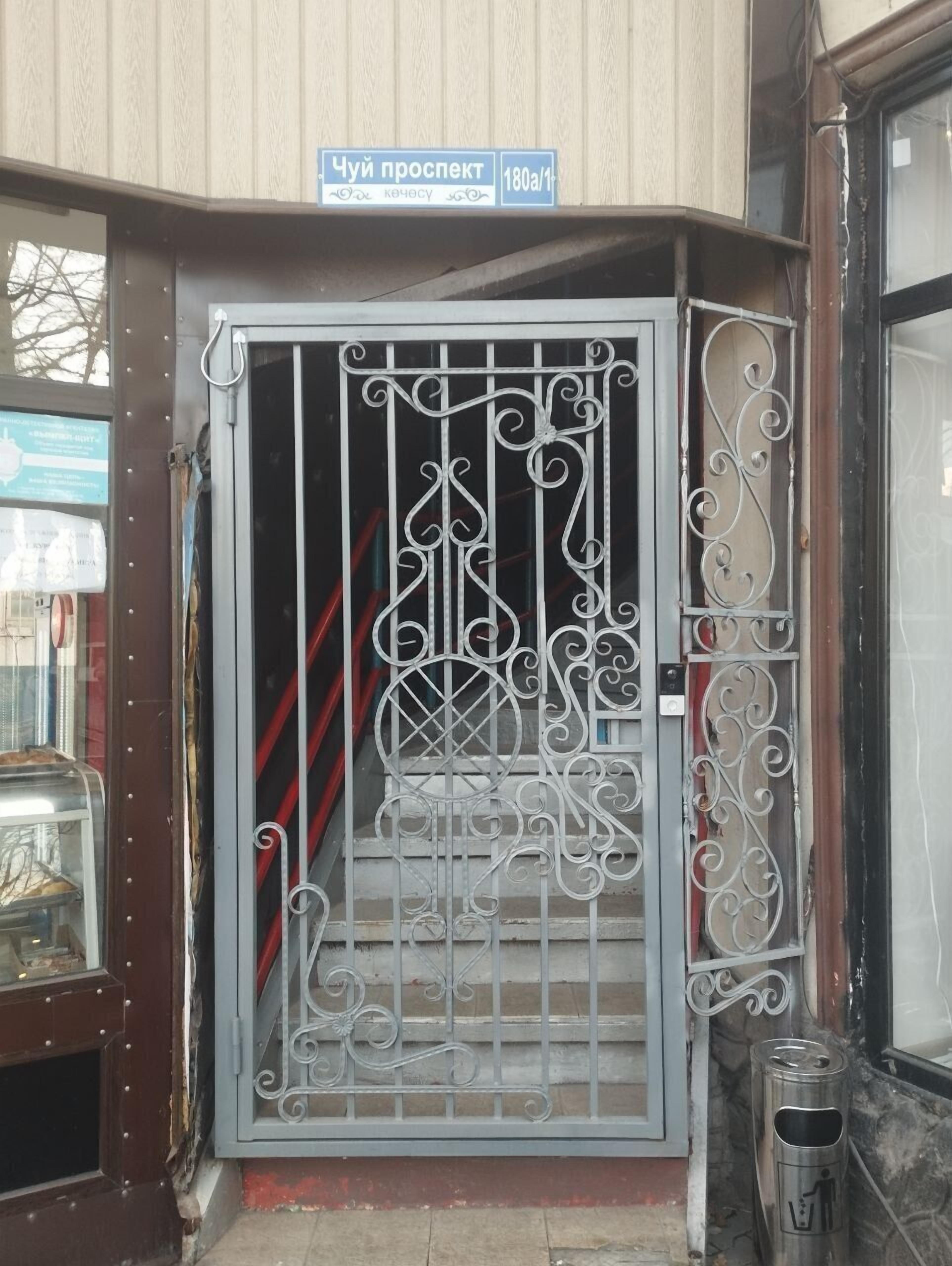 A metal gate with intricate designs, a sign above it, and a trash bin beside the gate.