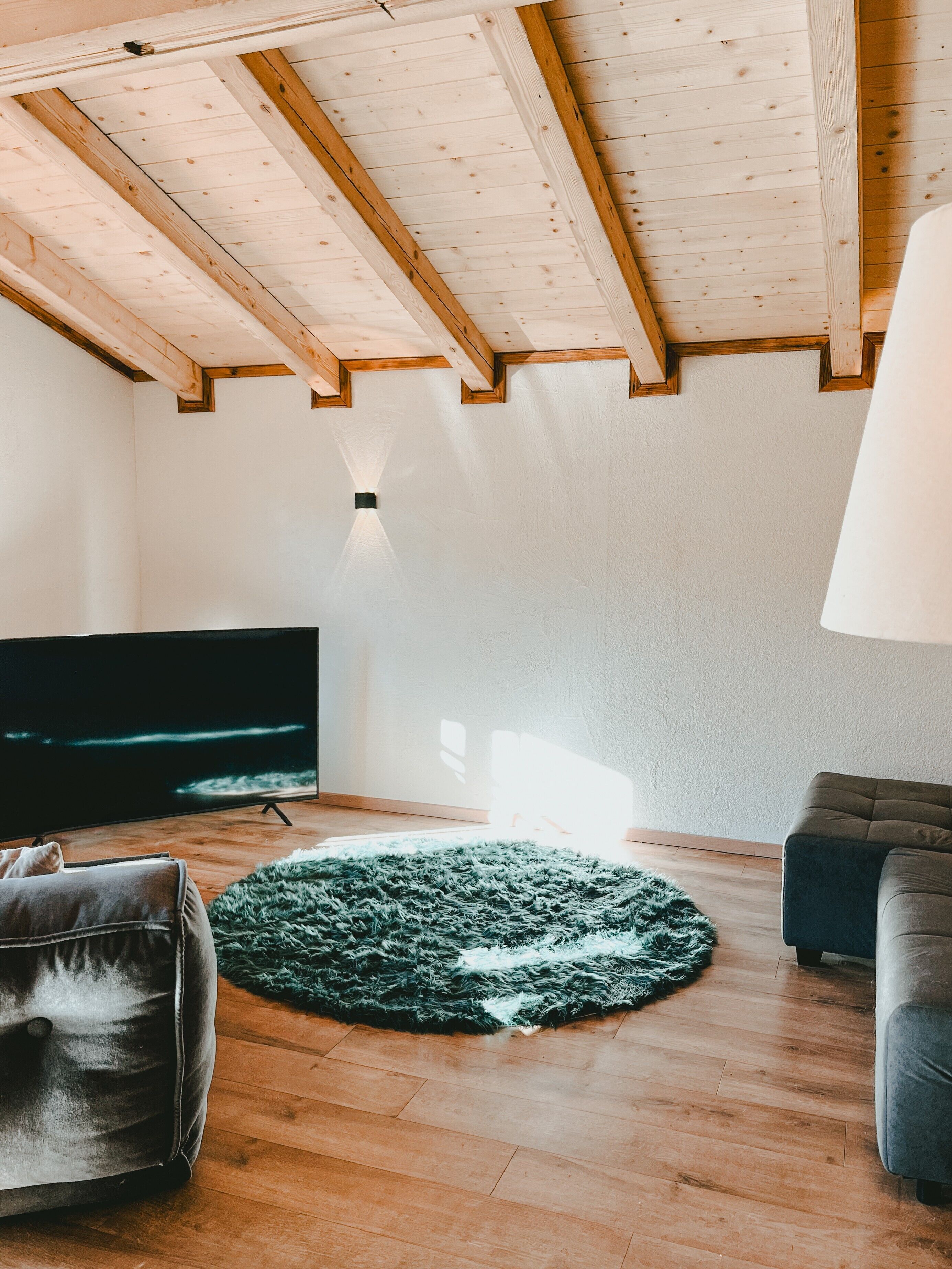 Un salon moderne avec des poutres en bois, un téléviseur à écran plat, un tapis vert et un canapé.