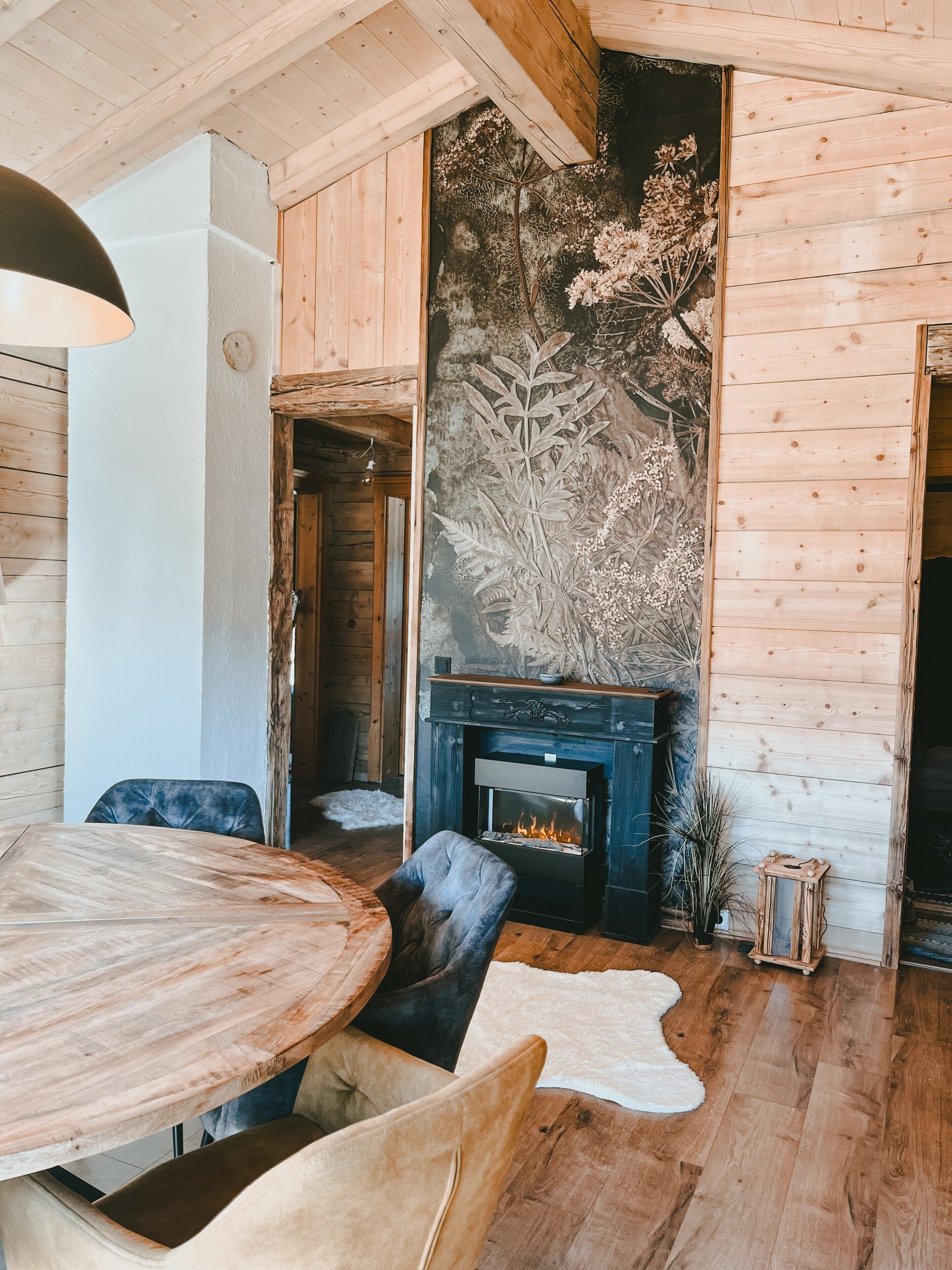 Ein gemütliches Zimmer mit Holzboden, einem runden Esstisch und einem Kamin mit dekorativer Wandmalerei.