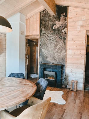 Um quarto acolhedor com piso de madeira, uma mesa de jantar redonda e uma lareira com um mural decorativo na parede.