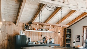 A kitchen with wooden beams, a central island, bar stools, and various kitchen appliances. - Apartment 'Katie' with Mountain View, Private Terrace and Wi-Fi (Hopfgarten)