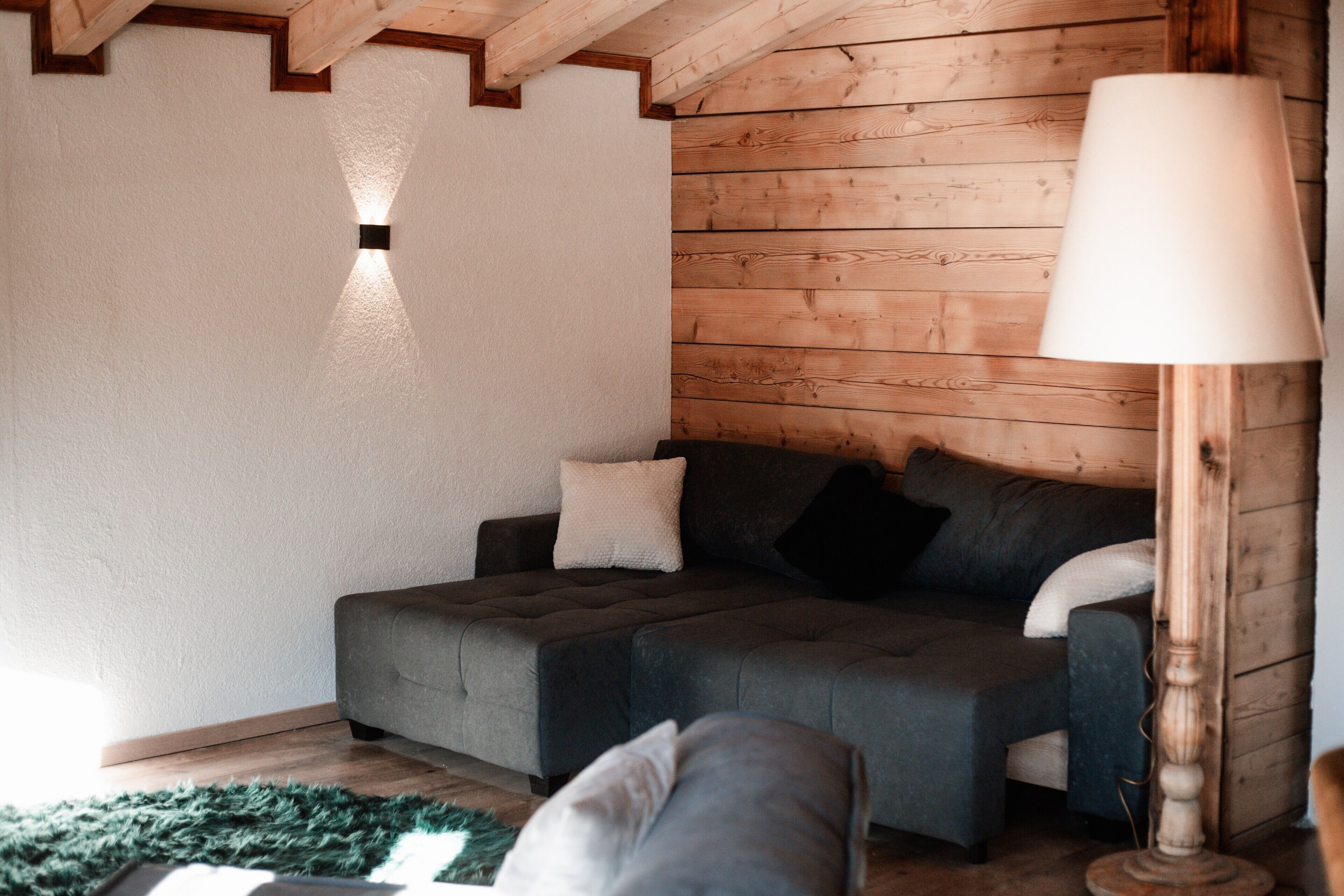 A cozy room with a sofa, a lamp, and wooden walls.
