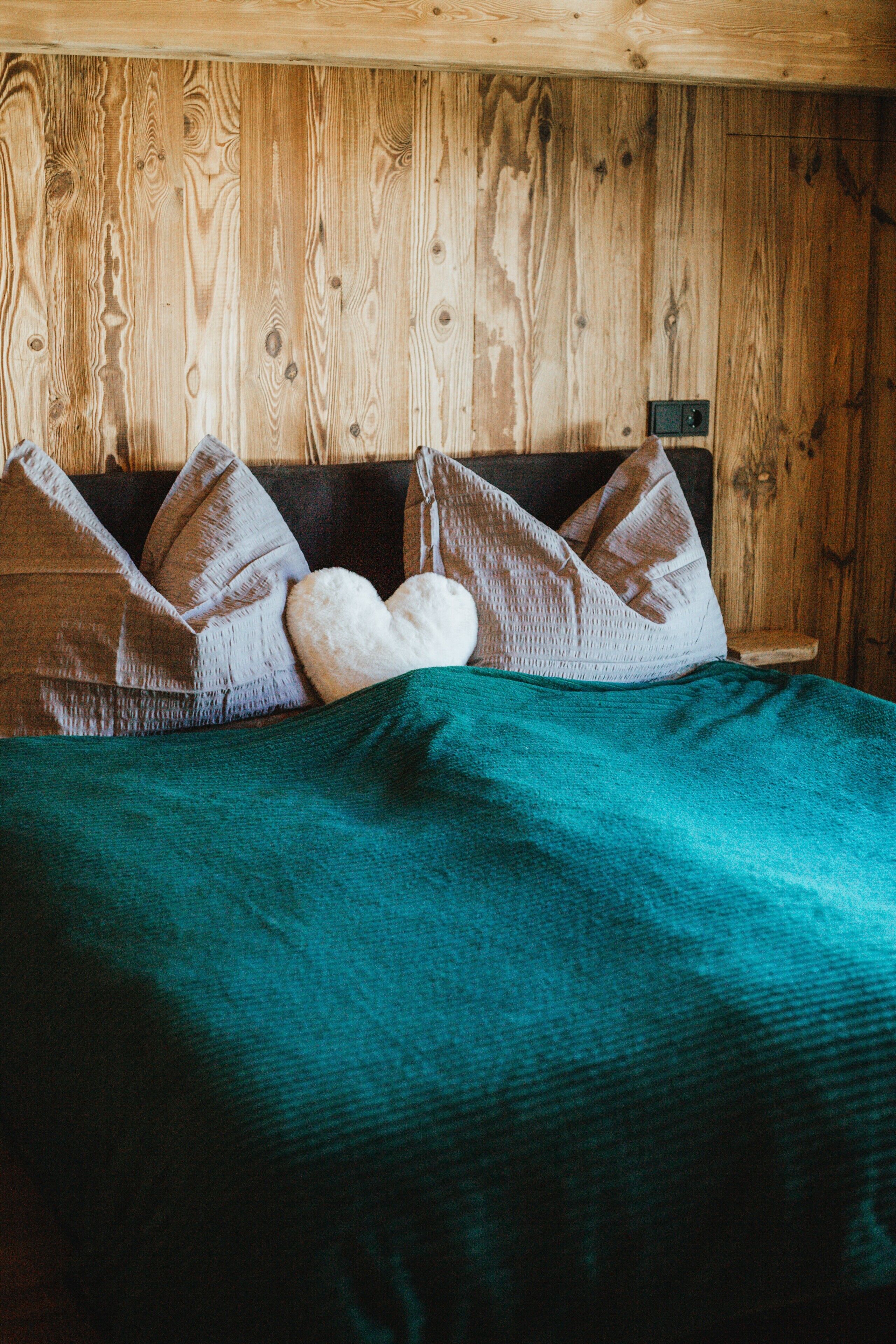 Ein Zimmer mit Holzwänden, einem Bett, Kissen und einer Decke.