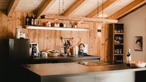 A kitchen with wooden walls, a hanging light fixture, and a variety of kitchenware and appliances. - Apartment 'Katie' with Mountain View, Private Terrace and Wi-Fi (Hopfgarten)
