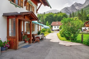 A building with a wooden facade, a covered outdoor seating area, and a paved pathway leading to a mountain backdrop.
