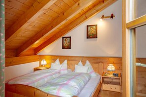 Ein Schlafzimmer mit Holzboden, einem Bett mit farbenfroher Bettdecke, zwei Wandlampen und einem Nachttisch mit Lampe.