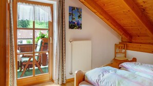 Un dormitorio con techo de madera, una cama con colcha colorida, una silla, un radiador y una ventana con cortinas.