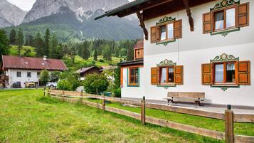 A traditional chalet with wooden shutters, a bench outside, and a mountainous backdrop.