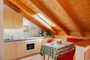 Une cuisine avec des meubles en bois, un poêle et une table à manger recouverte d’une nappe à carreaux.