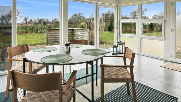A modern dining area with a round table, four chairs, and large windows offering a view of the outdoors. - "Thrine" - 24km from the sea by Interhome (Bredebro)