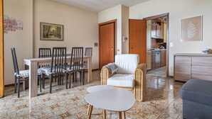 Un coin repas avec une table et des chaises, un fauteuil en osier et, au fond, une cuisine.