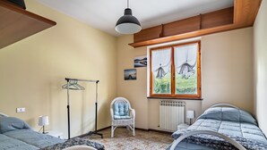 Une chambre avec deux lits, une chaise, un radiateur et une fenêtre avec des rideaux.