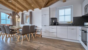 A modern kitchen with white cabinets, a wooden dining table with chairs, and a view of the outdoors.