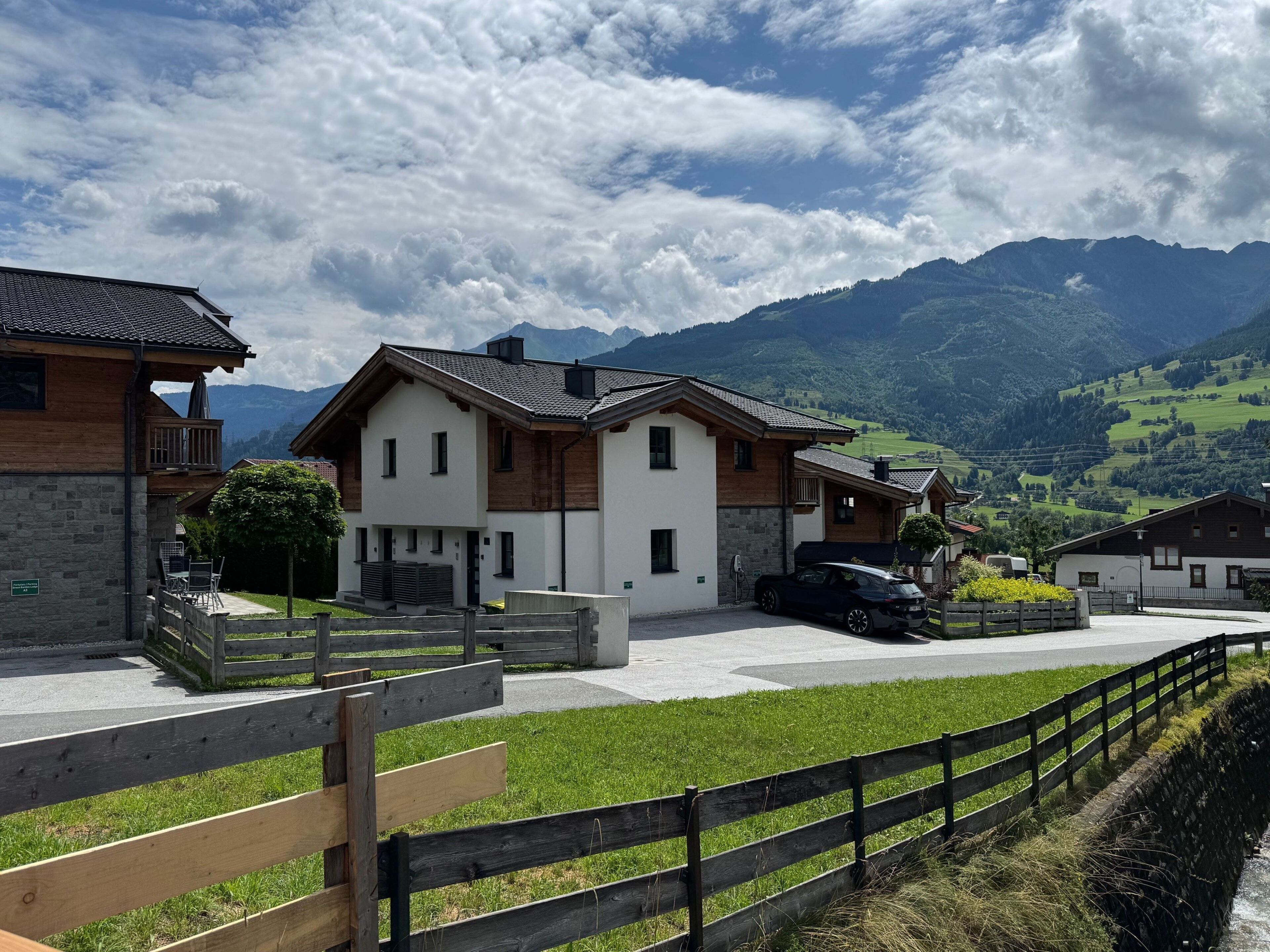 Una hilera de casas modernas con fachada de piedra, terraza de madera y vistas a montañas al fondo.
