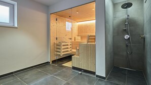 A modern bathroom with a wooden sauna, a shower area, and a tiled floor.