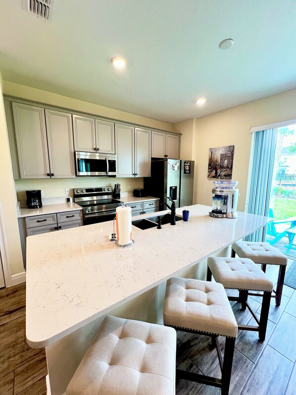 A modern kitchen with a large island, stainless steel appliances, and a view of the outdoors.