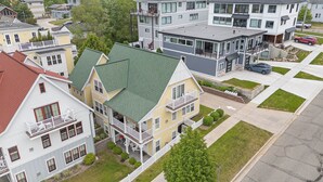 A residential area with multiple houses, including a two-story house with a green roof and a balcony, and a modern two-story house with a balcony and a driveway. - 🌊 Lake Effect – Channel Views • Pool • Deck • Steps to Beach & Downtown ➠ 27 (Grand Haven)