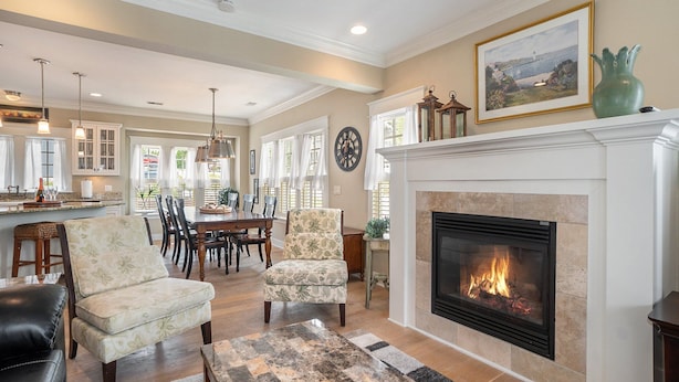 A spacious living room with a fireplace, dining area, and kitchen in the background. - 🌊 Lake Effect – Channel Views • Pool • Deck • Steps to Beach & Downtown ➠ 27 (Grand Haven)