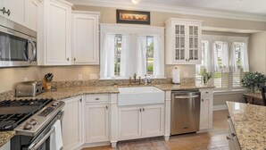 A kitchen with white cabinets, a stainless steel dishwasher, a gas stove, and a microwave. - 🌊 Lake Effect – Channel Views • Pool • Deck • Steps to Beach & Downtown ➠ 27 (Grand Haven)