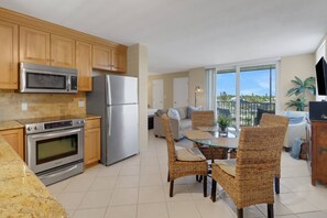 A modern kitchen with stainless steel appliances, a dining area with wicker chairs, and a balcony with a view.