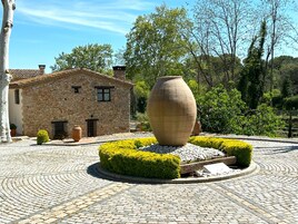 Un edificio de piedra con tejado de tejas, rodeado por un patio circular adoquinado con una gran maceta de barro en el centro.