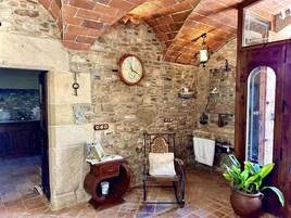 Una habitación rústica con paredes de ladrillo visto, una silla de madera, una mesita auxiliar de madera, un reloj y una planta en maceta.