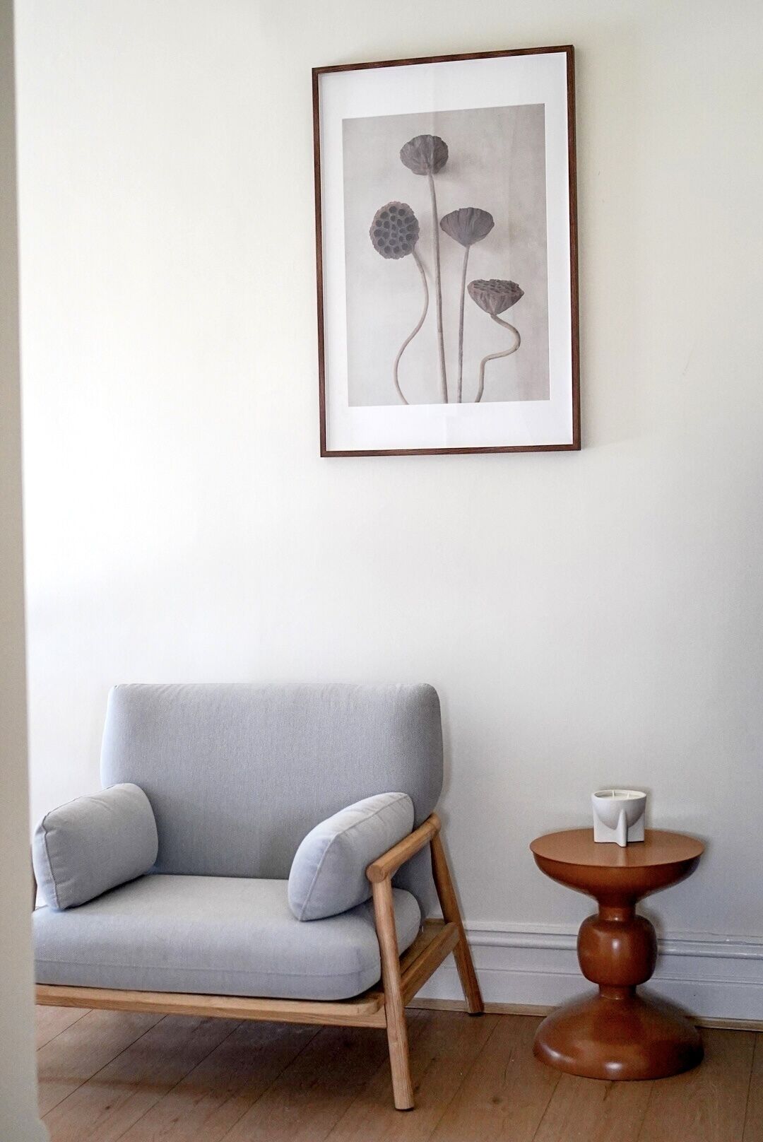 Une pièce avec un canapé gris, une chaise en bois, une petite table ronde en bois et une œuvre d’art encadrée accrochée au mur.