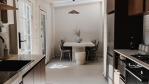 A modern kitchen with a central island, a dining table with chairs, and a hanging light fixture.