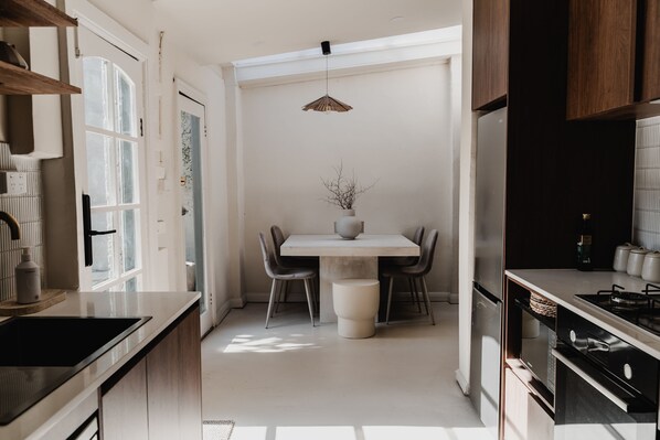 Een moderne keuken met een centraal kookeiland, een eettafel met stoelen en een hanglamp.