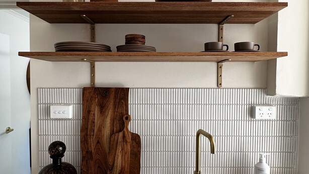 A kitchen with a black sink, wooden shelves above, and a tiled backsplash.