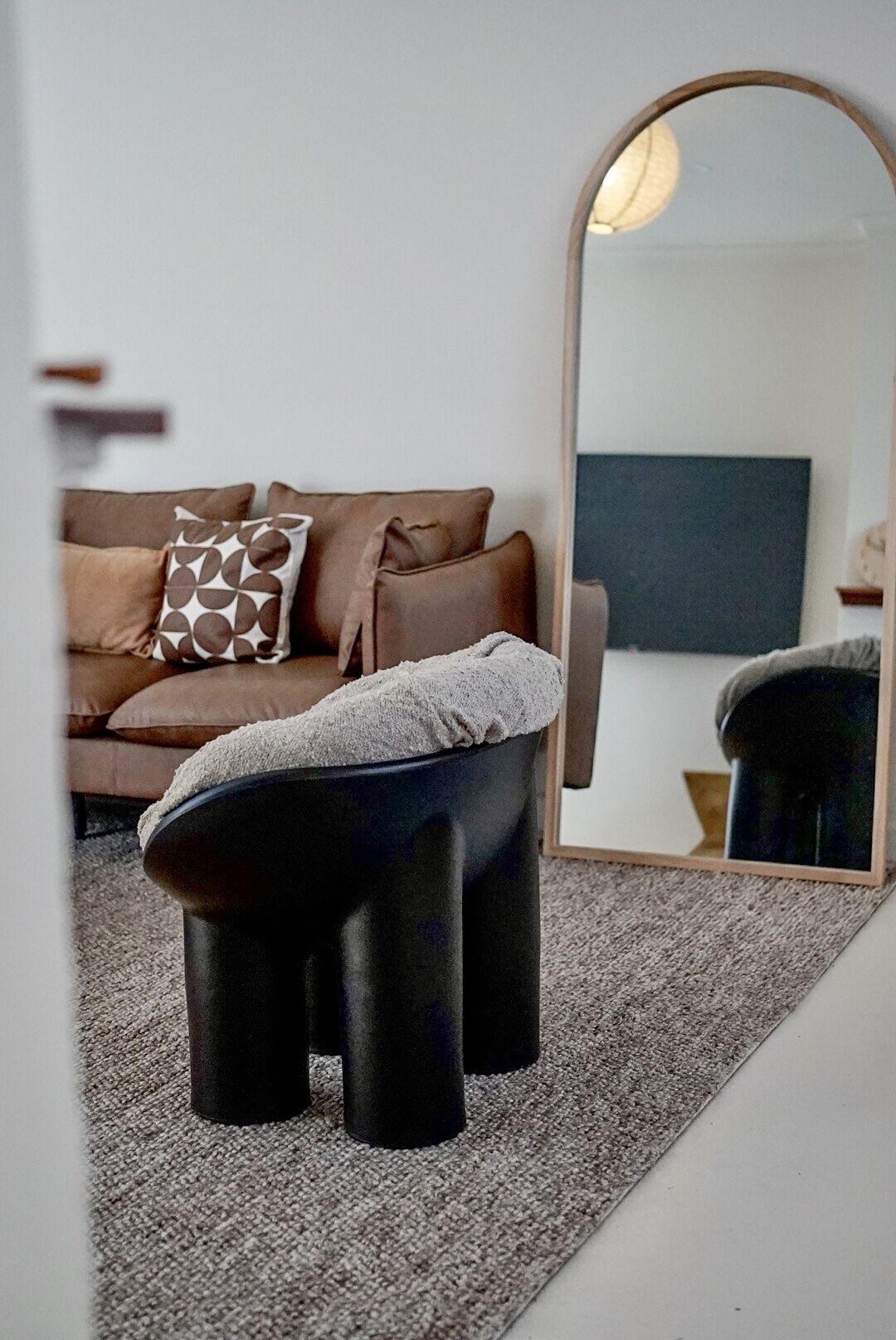 A modern living room with a sofa, a round mirror, and a small stool.