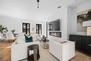 Ein modernes Wohnzimmer mit Kamin, weißen Sofas, einem Couchtisch und einem Essbereich mit Stühlen und einem Tisch.