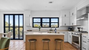 Una cucina moderna con mobili bianchi, un'ampia finestra, un'isola centrale con sgabelli e un forno integrato.