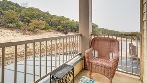 A balcony with a wicker chair, a metal table, and a view of a beach and trees. - Jonestown Condo on Lake Travis w/ 2 Balconies! (Jonestown)