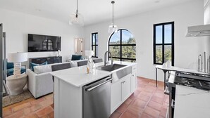 A modern kitchen with a central island, a dining area, and a living space with a sofa and TV. - Villa 6 / 3BR / Pool / Hot tub / Firepit / Cornhole (Spicewood)