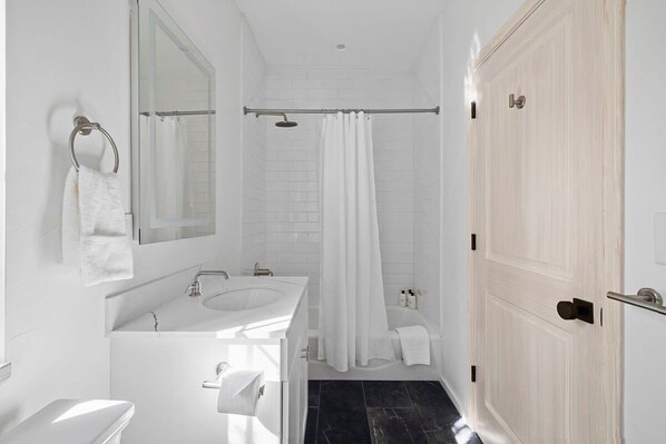 Une salle de bain moderne avec un lavabo blanc, un miroir et des toilettes, une douche avec un rideau et une porte en bois.