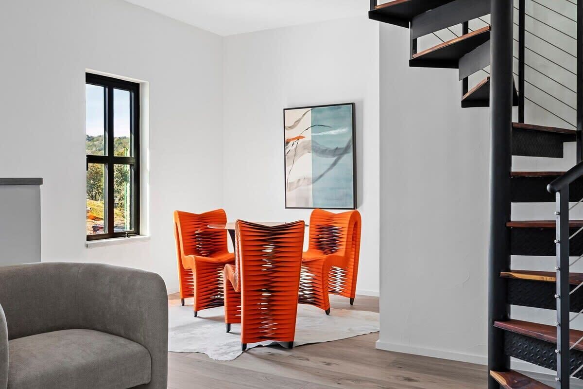 En modern inredning med en trappa, en grå soffa och orangefärgade stolar.