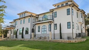 A large, multi-story house with a spacious front yard, a covered patio, and a stone retaining wall. - Villa 6 / 3BR / Pool / Hot tub / Firepit / Cornhole (Spicewood)