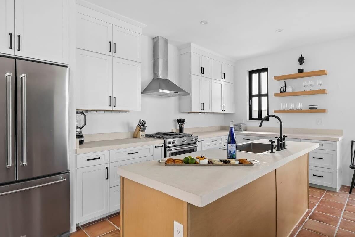 A modern kitchen with white cabinets, stainless steel appliances, a central island, and a window overlooking the room.