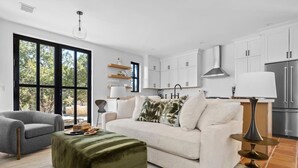 Un moderno salón con sofá, una mesa de centro y una lámpara. Cuenta con una zona de cocina con armarios y un refrigerador.