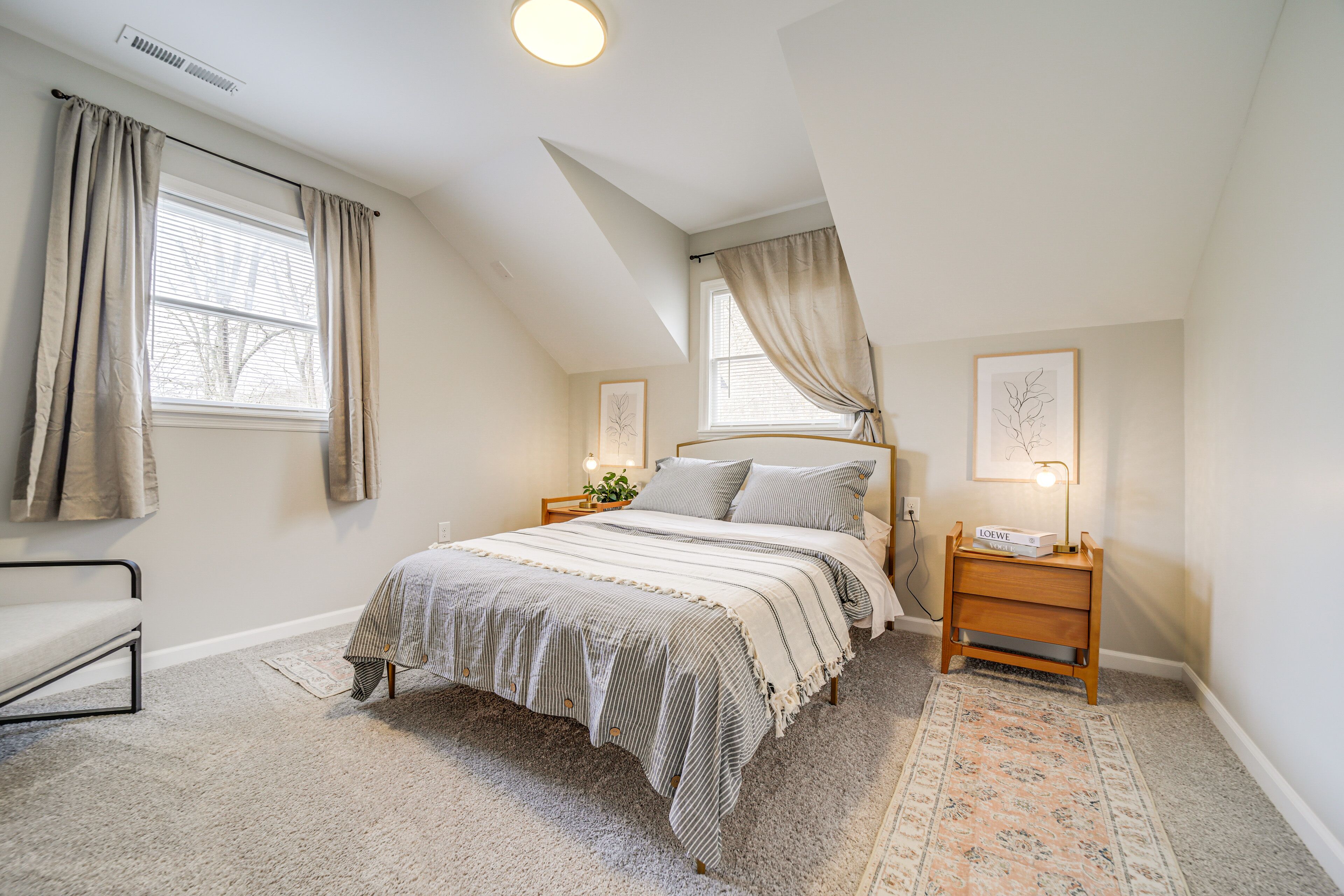 Une chambre avec un grand lit, deux tables de chevet, une commode, une chaise, une fenêtre avec des rideaux et une lampe fixée au mur.
