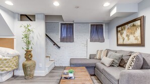 Un salón con un sofá gris, una mesa de centro de madera, un jarrón grande con una planta y un mapa del mundo en la pared.