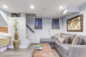 Ein Wohnzimmer mit einem grauen Sofa, einem Holztisch, einer großen Vase mit Pflanze und einer Weltkarte an der Wand.