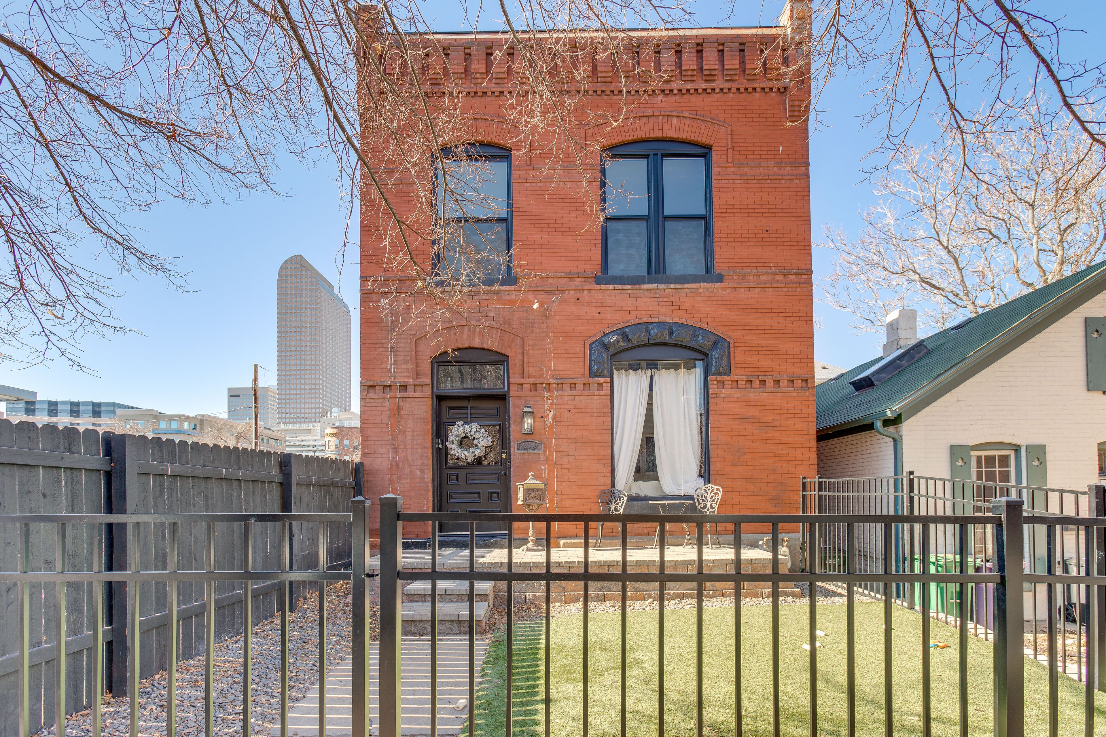 A red brick building with a front door, two windows, and a small porch with a chair and table.