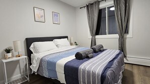A neatly made bed with a striped bedspread, a bedside table with a lamp, and two framed artworks on the wall.