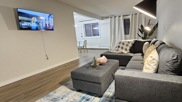 A modern living room with a grey sofa, a grey ottoman, and a flat-screen TV mounted on the wall.